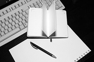 Keyboard, paper schedule, notebook, and pen laying on a table indicating or inferring the capturing of deep thought (e.g., knowledge-repo).